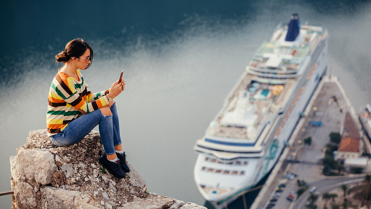 Woman on phone on top of cliff overlooking cruise ship
