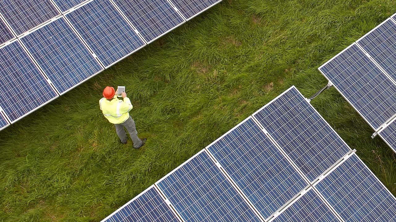 A technician works in a grass field between two solar panel arrays