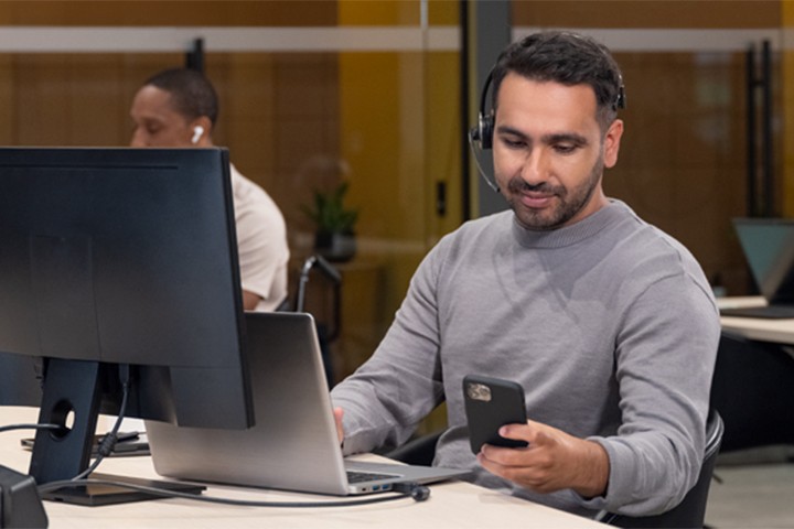 Customer service agent looking at smartphone while using a laptop
