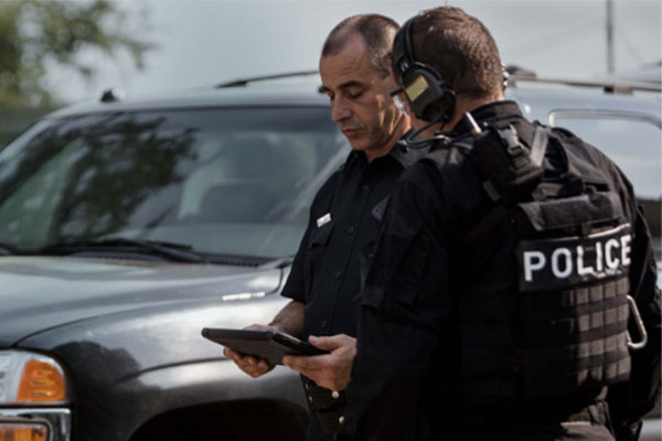 two white male police officers working on a tablet next to a police car