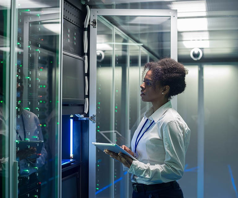 Medium shot of female technician working on a tablet in a data center full of rack servers running diagnostics and maintenance on the system