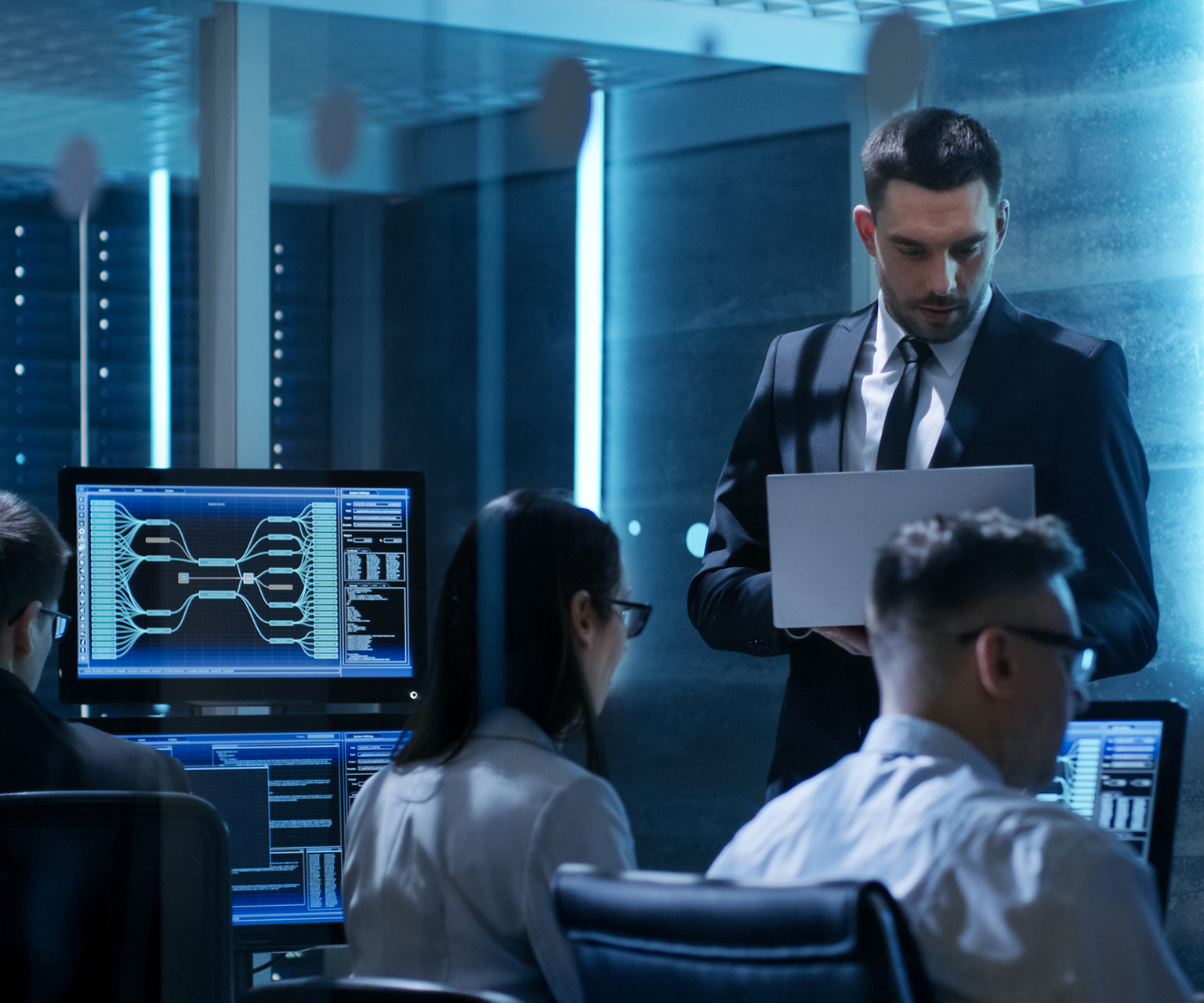 Professional IT Engineers Working in System Control Center Full of Monitors and Servers. Supervisor Holds Laptop and Holds a Briefing. Possibly Government Agency Conducts Investigation. 