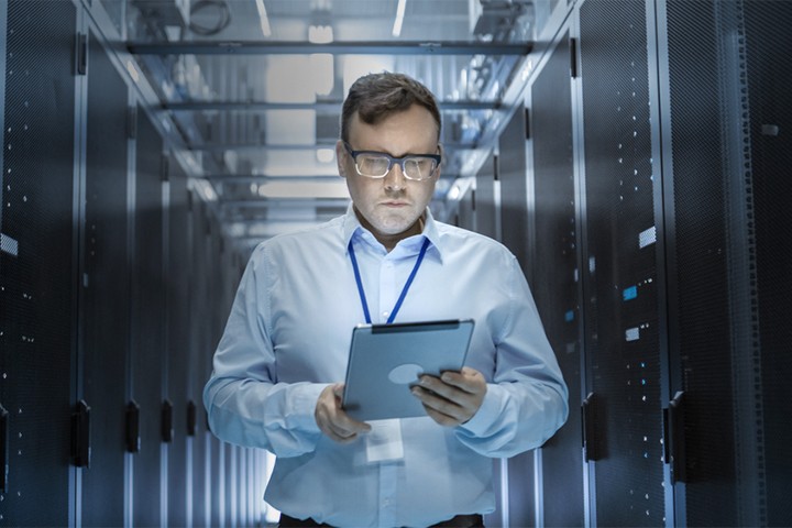 IT technician walks through sever room in data center while using a tablet