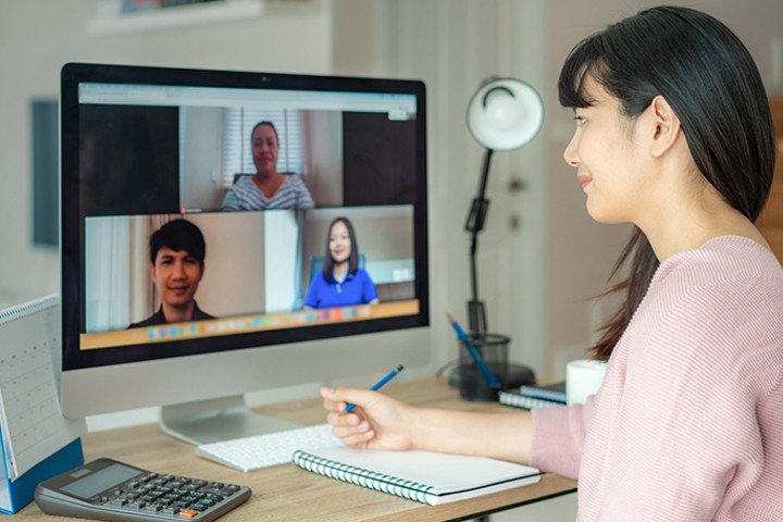 Woman taking notes while video conferencing from destop computer