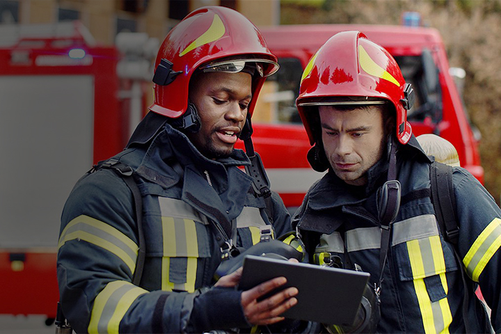Two male firefighters using a tablet while standing beside fire truck