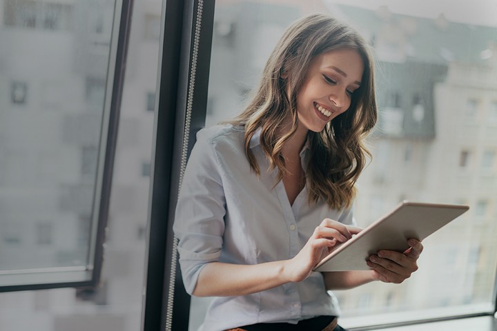 Woman using tablet while standing in front of office window