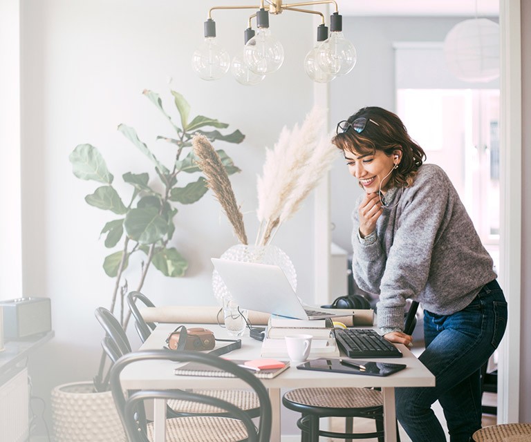 Woman standing over desk, smiling at computer