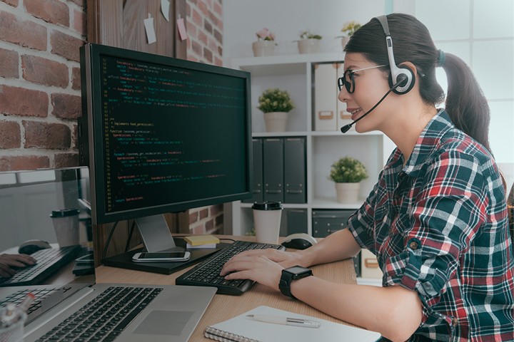 Computer engineer writing code on desktop while talking on a headset