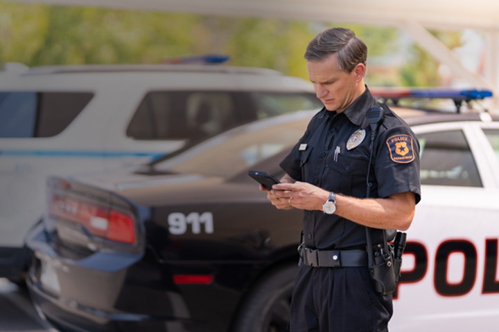 Police officer standing beside patrol vehicle while using smartphone
