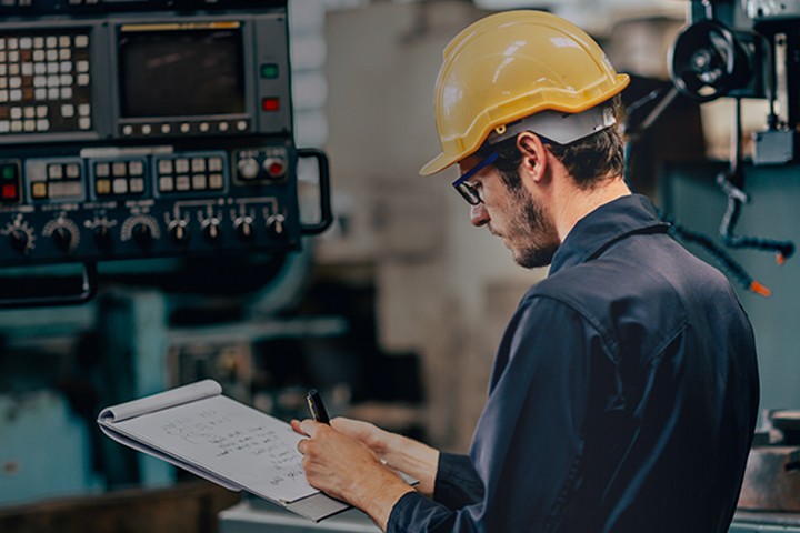 Technical engineer wearing hard hat operating heavy machinery in CNC factory