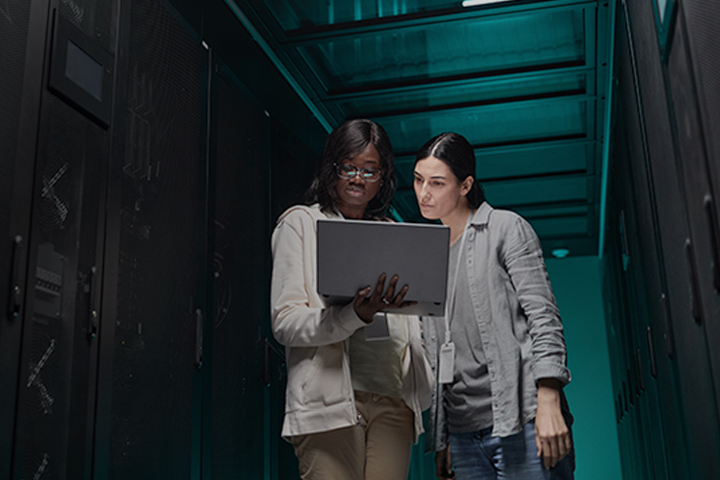 Two female IT engineers setting up network via laptop while standing in data center