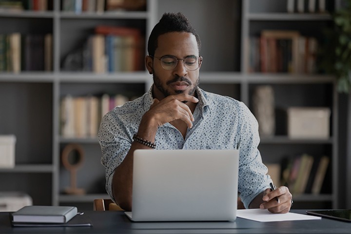 Thoughtful African American businessman looking at laptop screen, touching chin