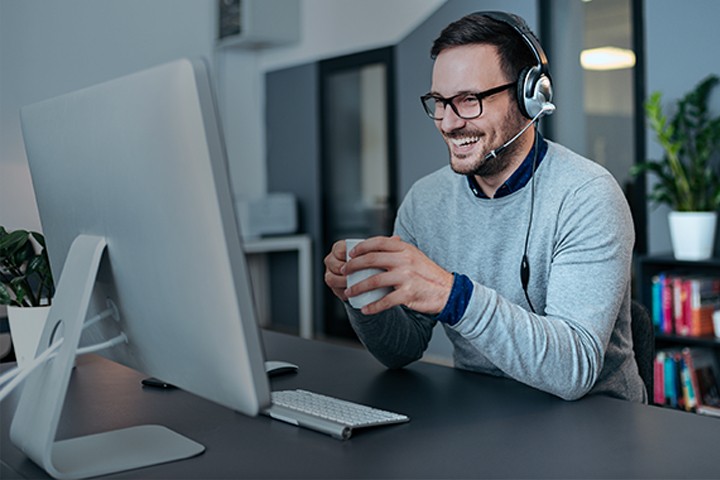 Remote contact center agent speaking with customer while wearing a headset and working from home on a desktop computer