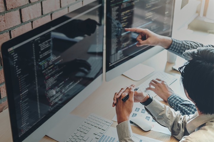 Program developer reviewing code on desktop computer with colleague