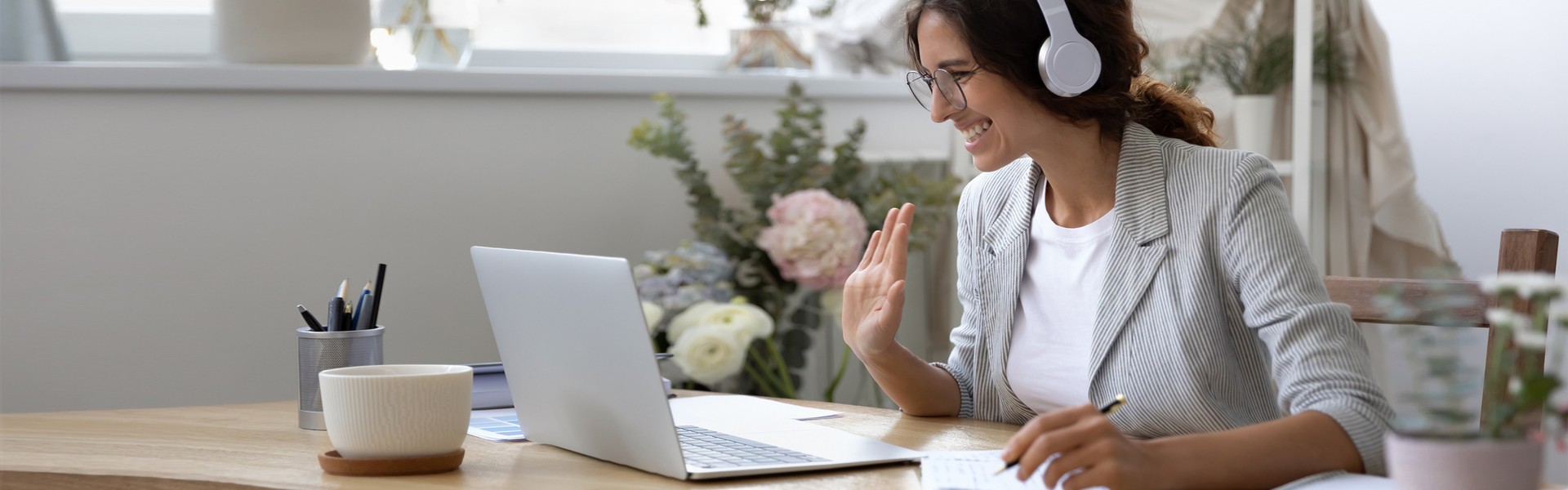 Woman chatting on webcam while wearing headphones and sitting in office space