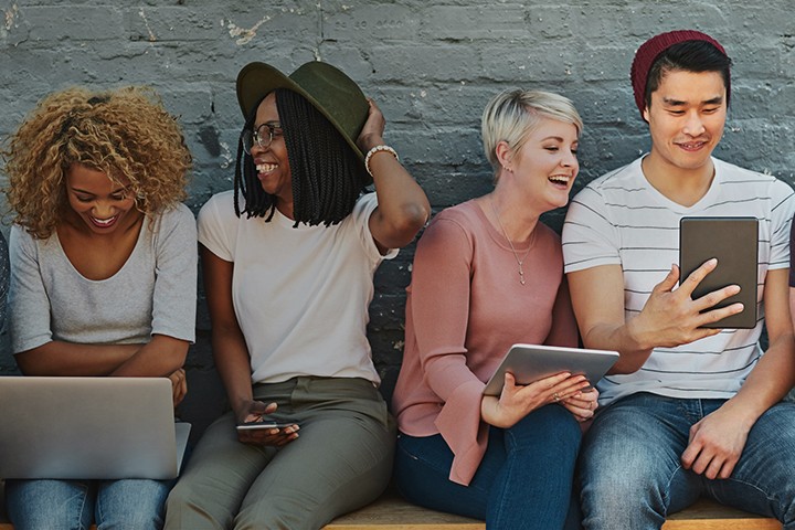 Group of friends sitting on bench outside with tablets and laptops