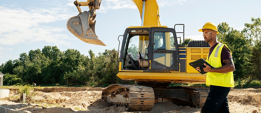 Construction worker using a tablet while standing beside construction equipment