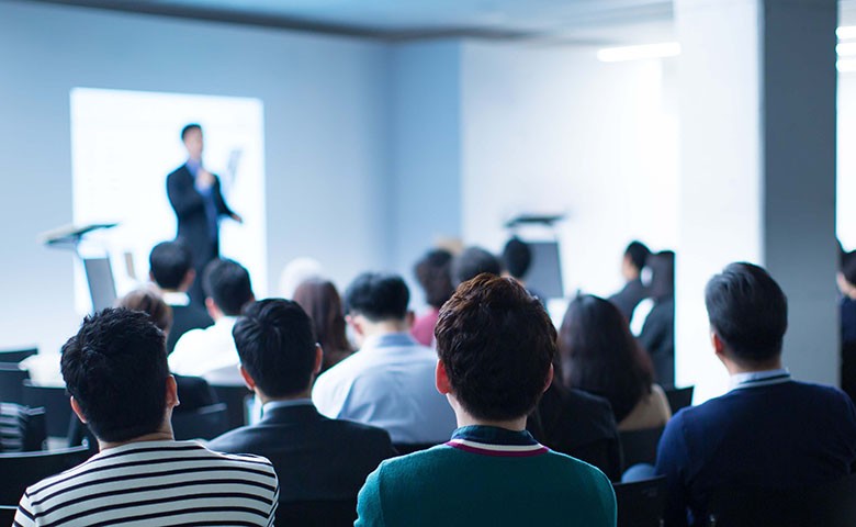 Presenter Presenting on Stage at Conference Meeting. Professional Lecture. Blurred De-focused Unidentifiable Presenter and Audience. Corporate Executive Manager Speaker. People Attendees