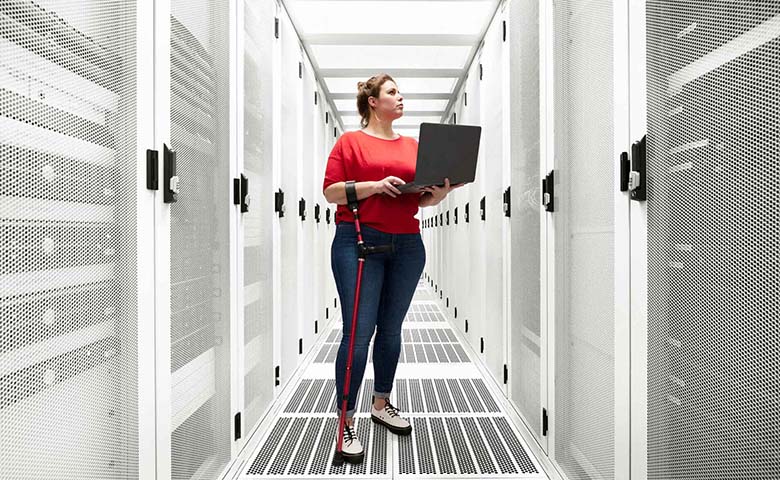 a woman in red shirt holding a laptop in a data center room