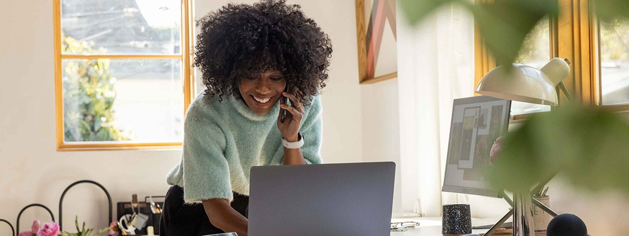 afro hair woman speaking on the mobile and looking at a laptop