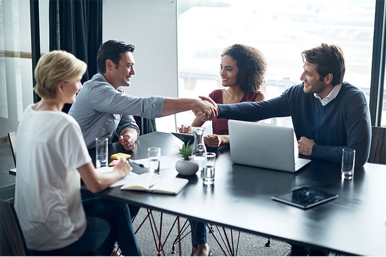 men and women having a meeting at the desk, two men shaking hands