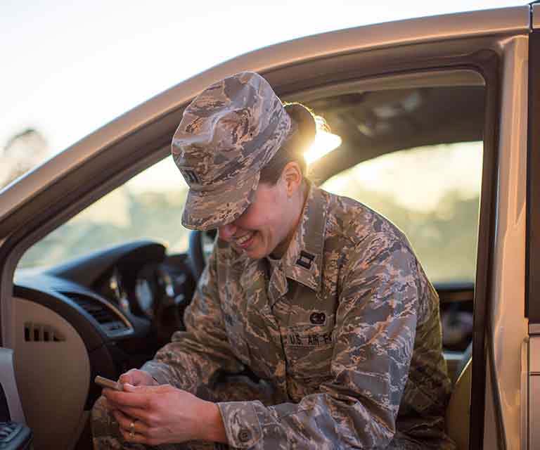 A military service member smiles as she looks at a smartphone