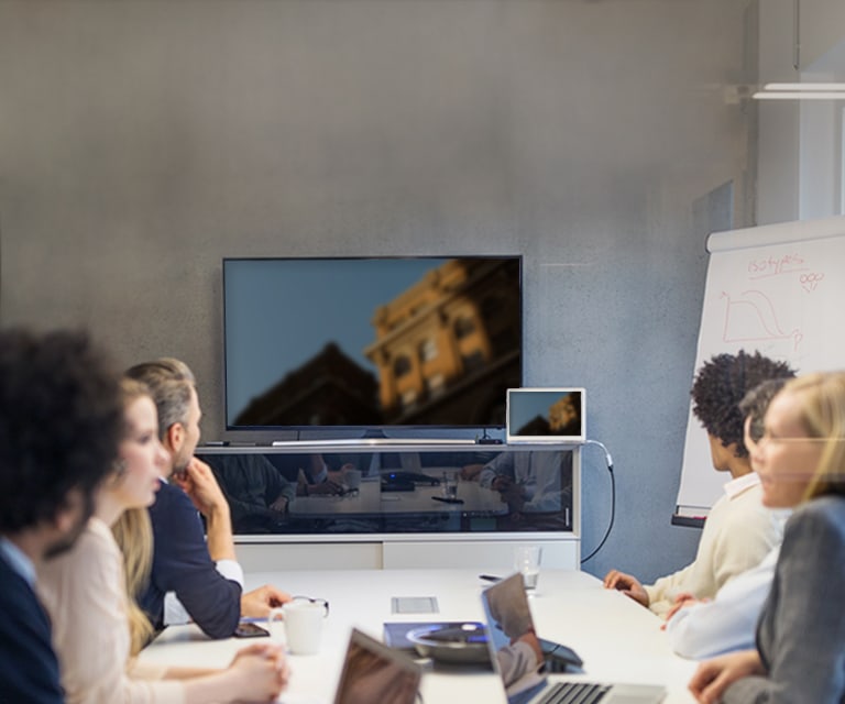 A group of coworkers at a conference table with a TV in the background.