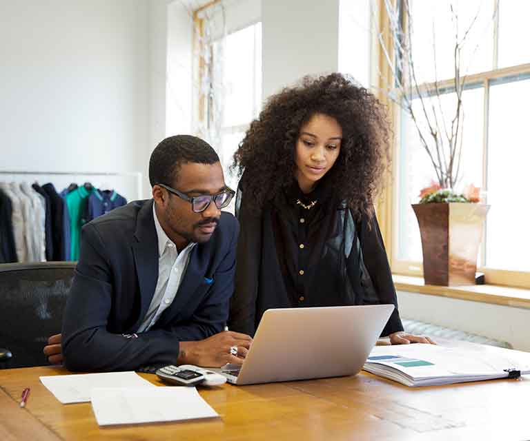 A man and woman in an office look at a laptop
