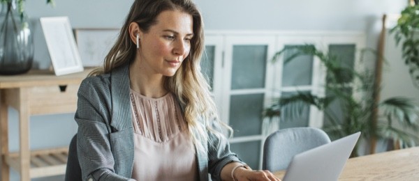 woman sitting at a table typing on a laptop with ear buds in her ear