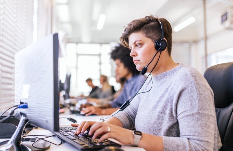 woman wearing a phone headset and typing on a keyboard while looking at desktop monitor