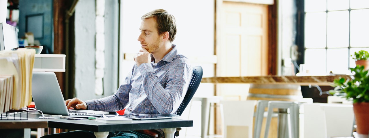 man sitting at table looking at laptop