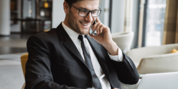 man on smartphone looking at laptop