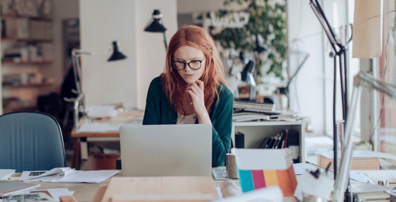woman wearing glasses sitting at desk looking at computer