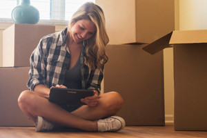 Woman sitting on floor with tablet surrounded by boxes